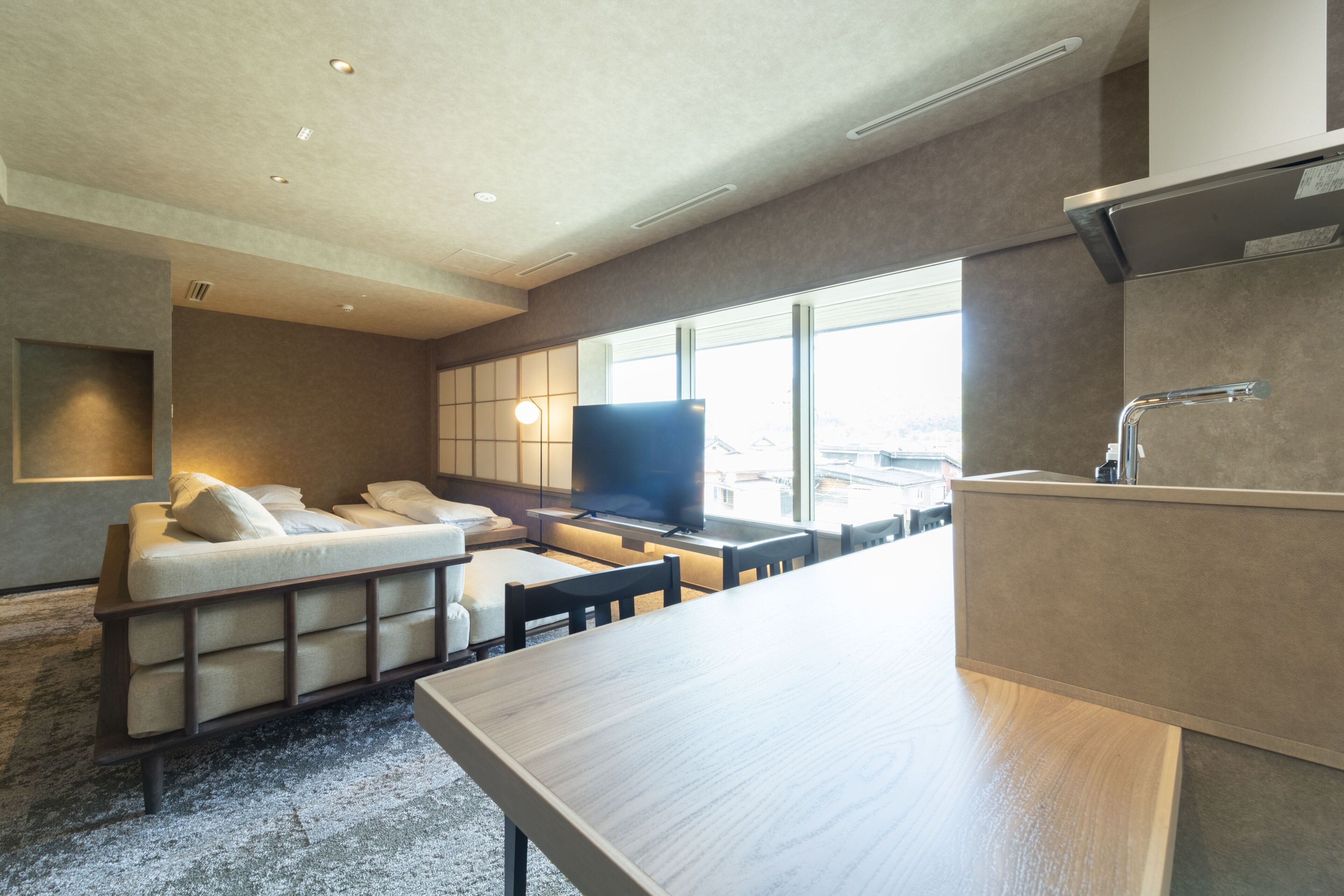 A modern hotel room with a sofa, a flat-screen TV, a dining table, and a kitchen area.