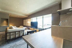 A modern hotel room with a sofa, a flat-screen TV, a dining table, and a kitchen area.