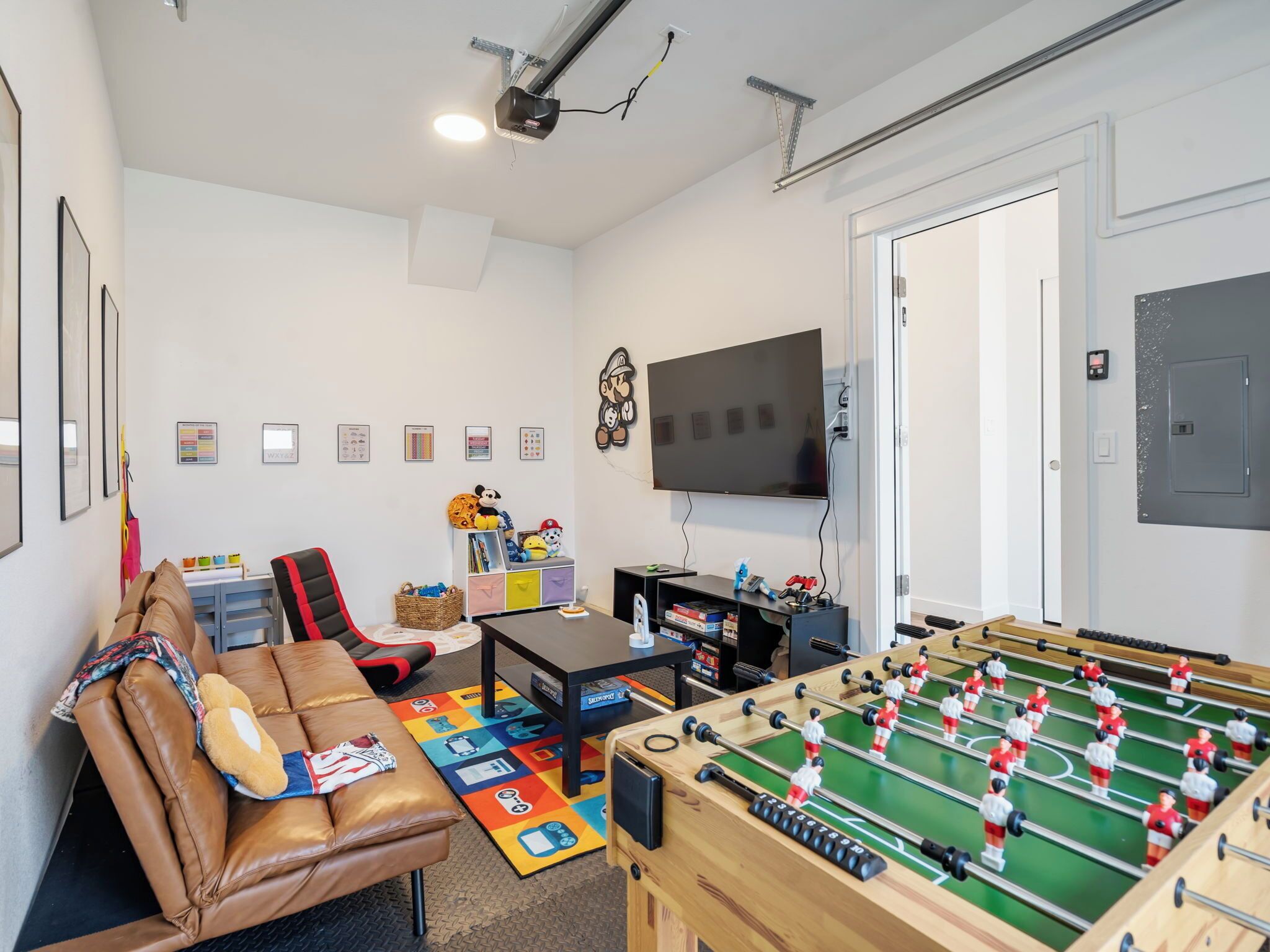 A room with a foosball table, a sofa, a television, and a wall-mounted shelf with toys.