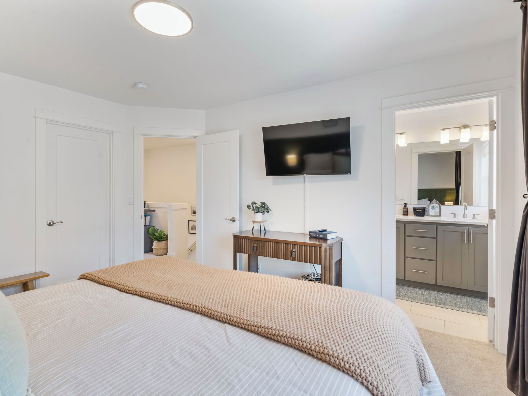 A bedroom with a bed, a dresser, a television, and a bathroom visible through an open door.