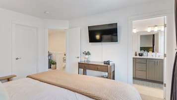 A bedroom with a bed, a dresser, a television, and a bathroom visible through an open door.