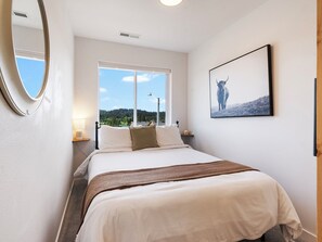 Habitación de hotel con cama, ventana con vistas, un cuadro enmarcado en la pared y un espejo.