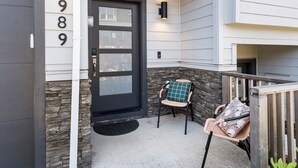 A front door with a black frame, a stone accent wall, and a small porch with two chairs. - Family friendly townhome + Game Room + King beds (Salem)