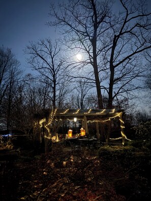 A gazebo with string lights, surrounded by trees and a wooden deck.