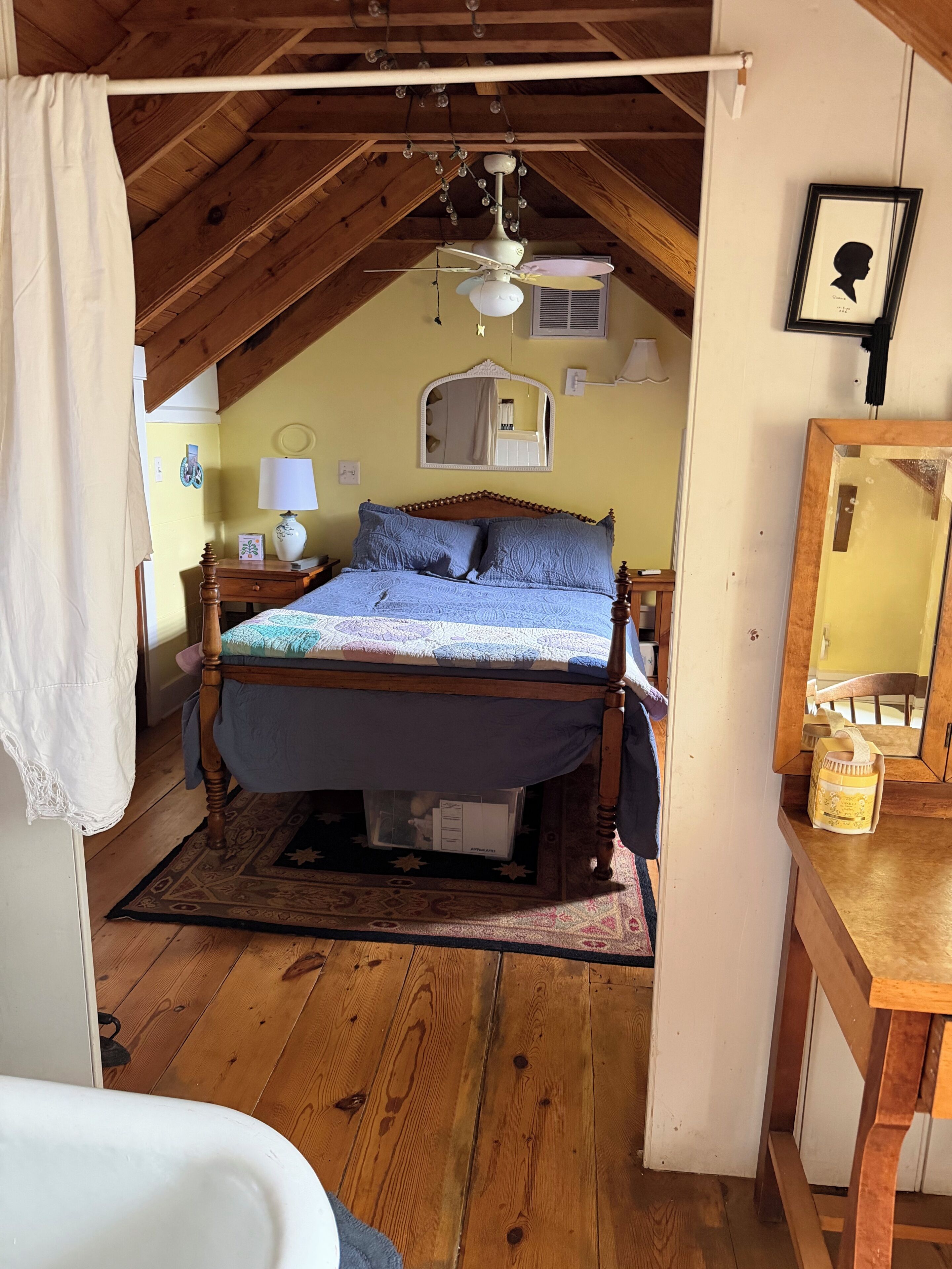 A bedroom with a wooden ceiling, a bed with a blue cover, a nightstand, a mirror, and a wooden dresser.