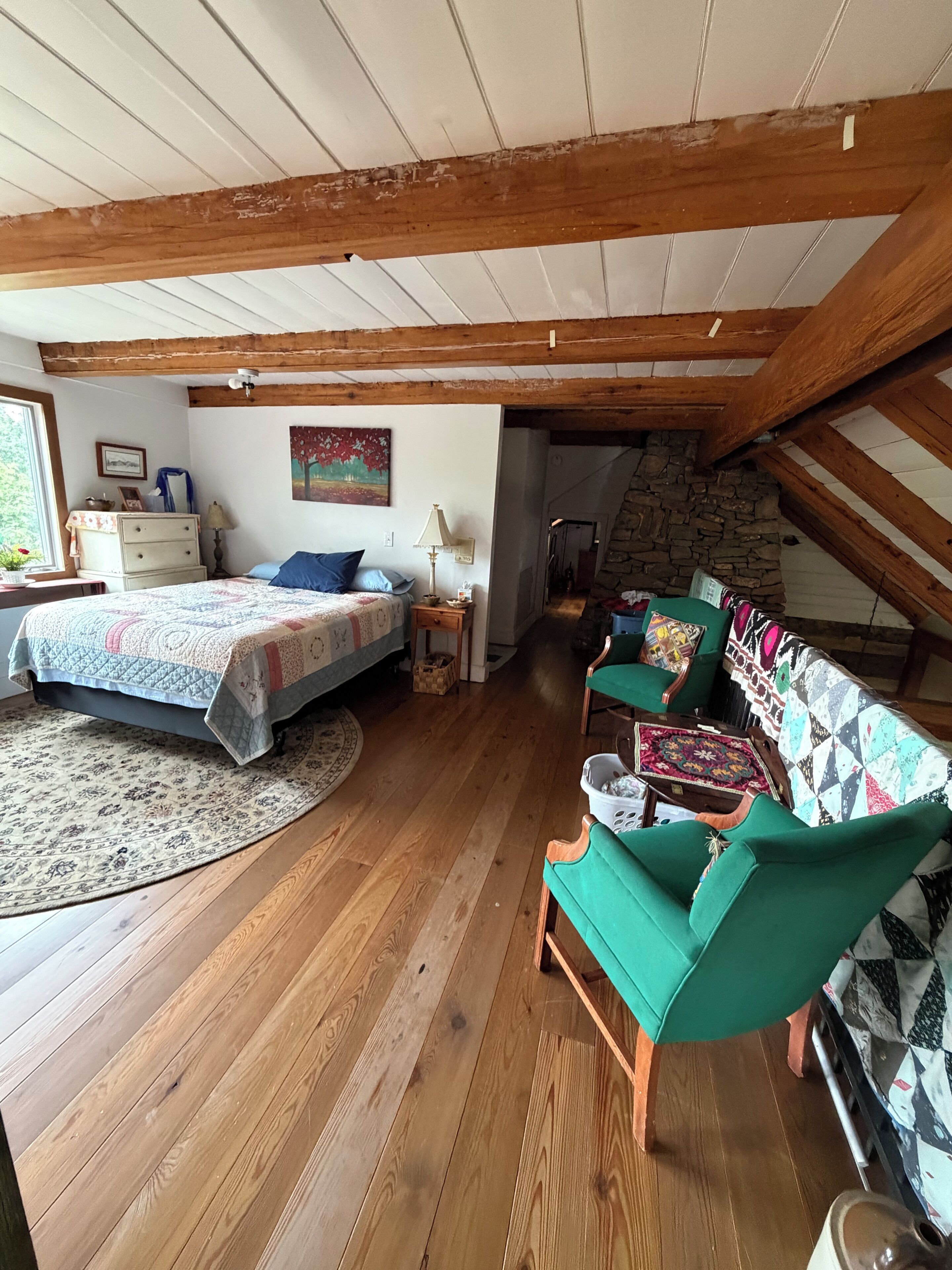 Un dormitorio estilo buhardilla acogedor con techo de madera, cama con colcha estampada, sillón verde y pared de piedra.