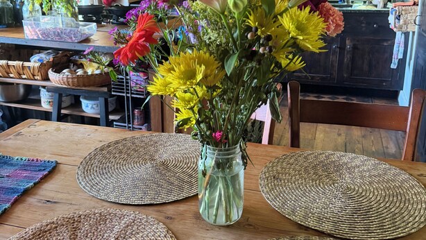 Una cocina con armarios de madera, ollas colgantes y un florero sobre una mesa con individuales tejidos.