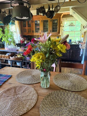 A kitchen with wooden cabinets, hanging pots, and a vase of flowers on a table with woven placemats.