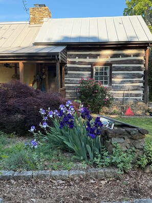 A rustic log cabin with a metal roof, a stone chimney, and a wooden porch.