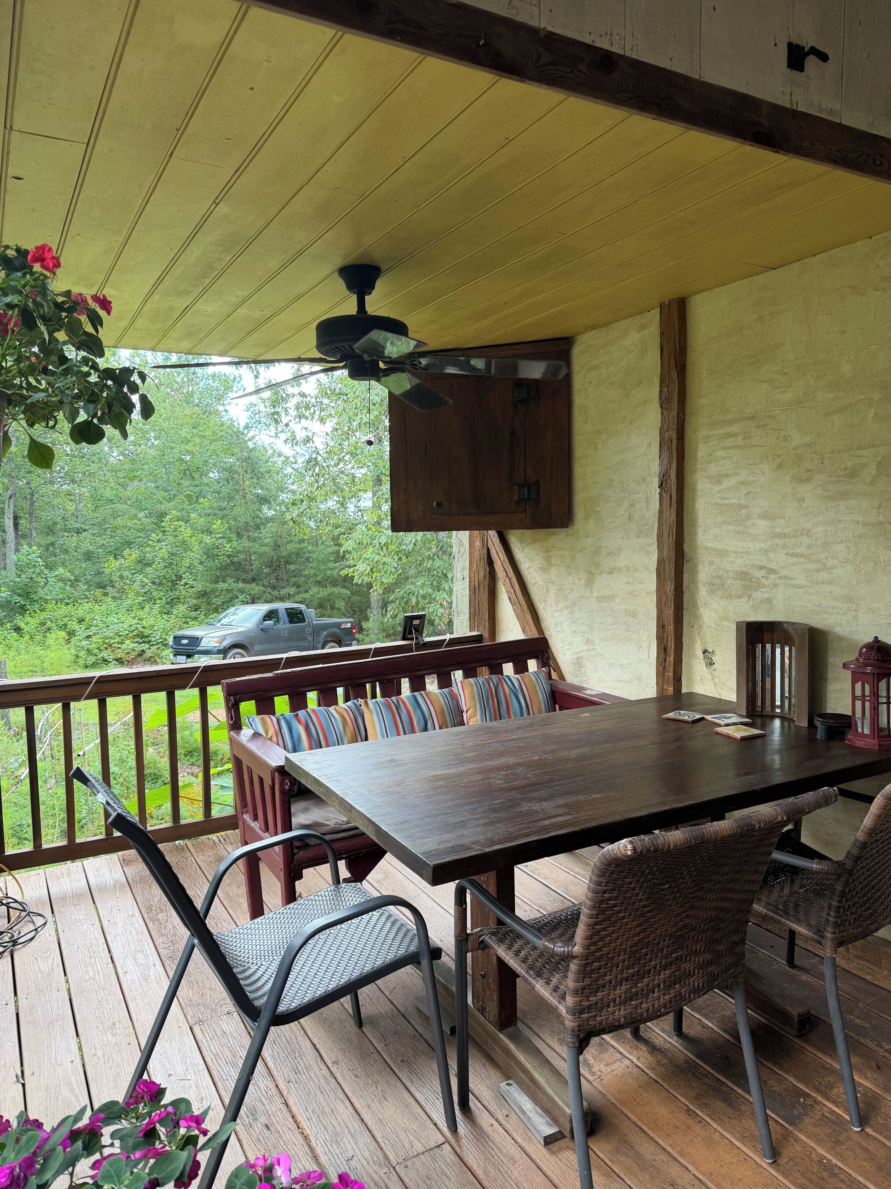 A covered outdoor seating area with a table and chairs, a ceiling fan, and a view of the outdoors.