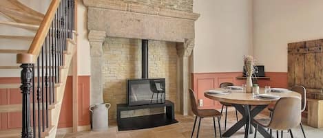 A dining area with a stone fireplace, a television on a stand, and a table set for four.
