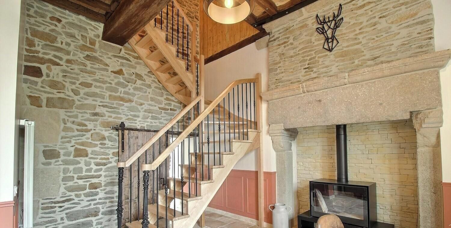 A stone wall, a wooden staircase with black railings, and a fireplace with a stone surround.