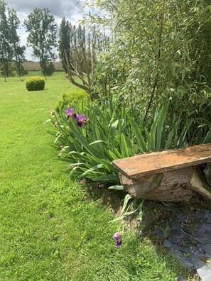 A garden with a wooden bench, green grass, and purple flowers. - Le Cerf - LANGAST - Vacation Rental (LANGAST)