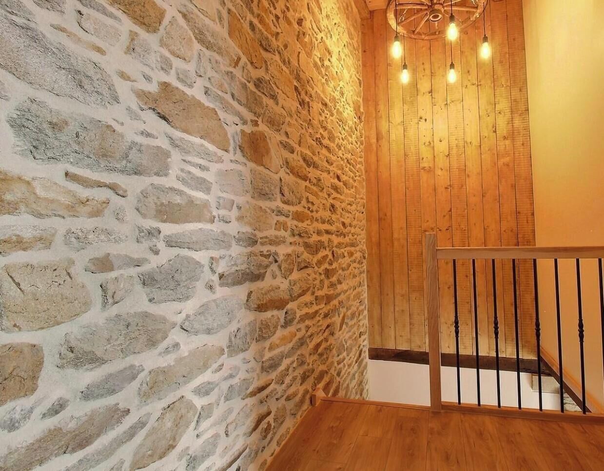A staircase with a wooden handrail leading to a room with a stone wall and a wooden ceiling.