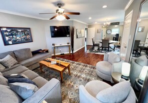A living room with a sofa, coffee table, and chairs, a television, and a dining area with a table and chairs.