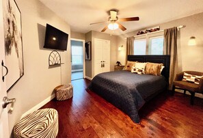 A bedroom with a bed, a ceiling fan, a TV, and a window with curtains.