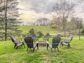 A grassy outdoor seating area with Adirondack chairs and a fire pit.