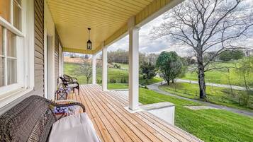 A covered porch with a wooden floor, a bench, and a view of a green landscape.