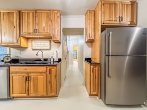 A kitchen with wooden cabinets, a stainless steel refrigerator, and a wall-mounted clock.