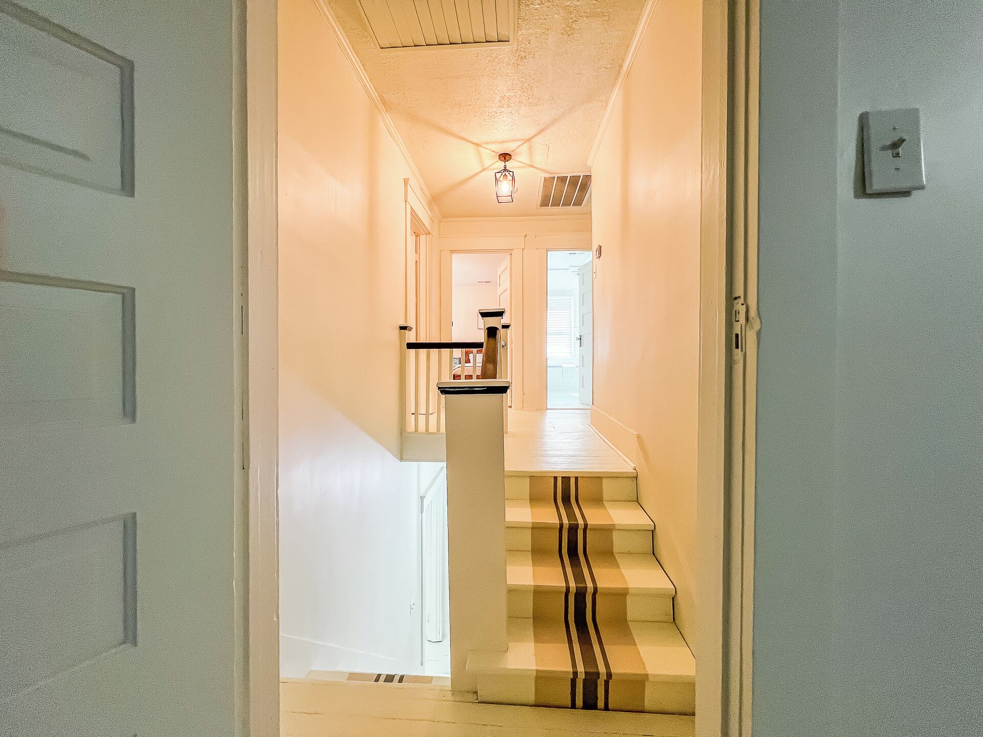 A hallway leading to a staircase with a striped carpet.