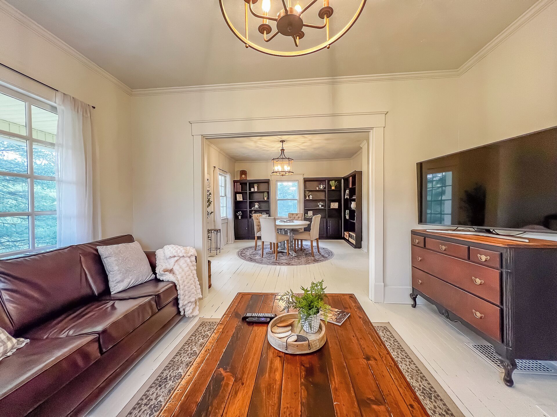 A spacious living room with a brown leather sofa, a wooden coffee table, and a TV stand.