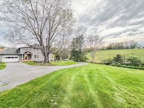 A residential property with a well-maintained lawn, a driveway leading to a garage, and a large tree in the foreground.