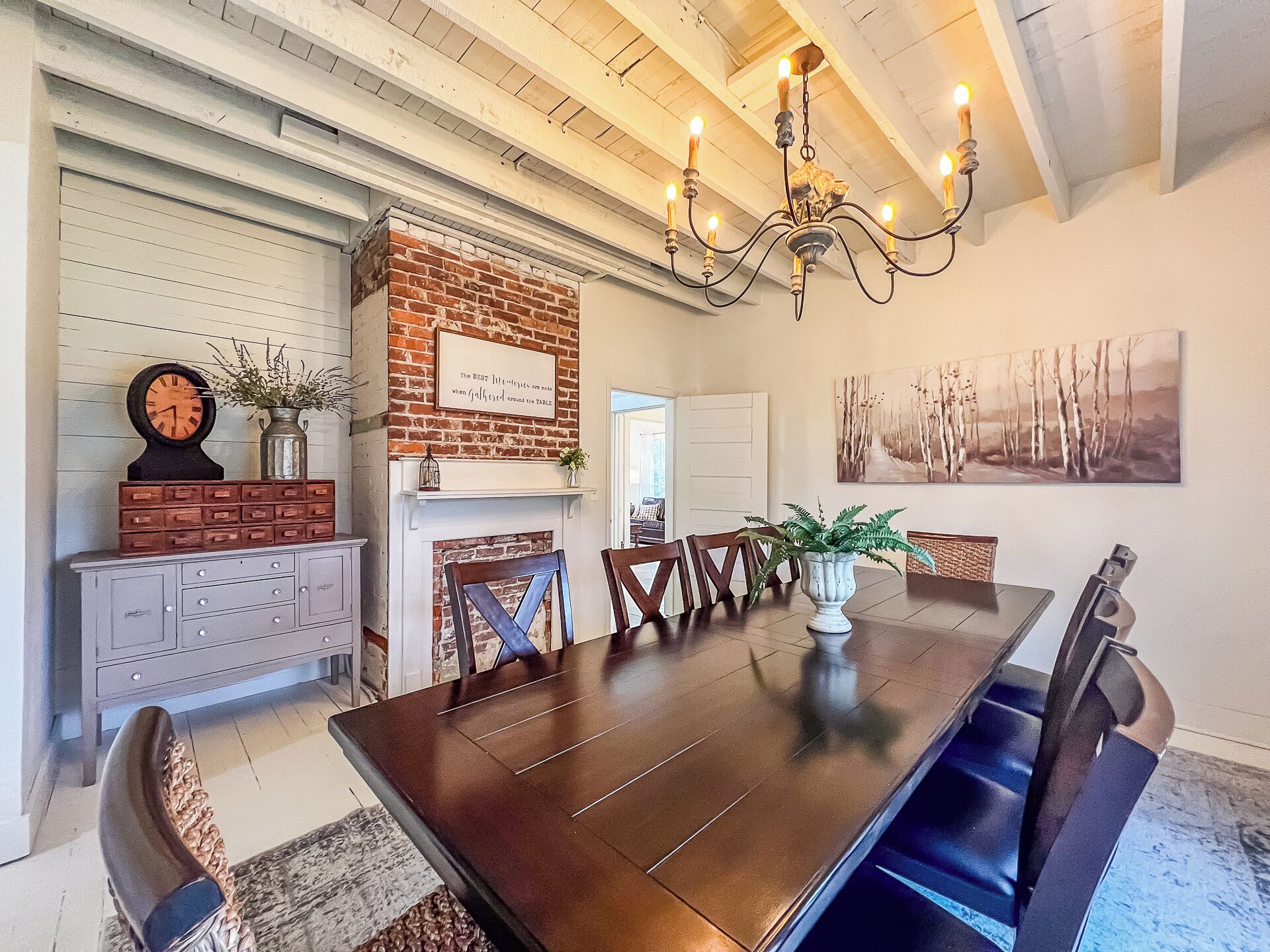A dining area with a brick accent wall, a chandelier, and a painting.