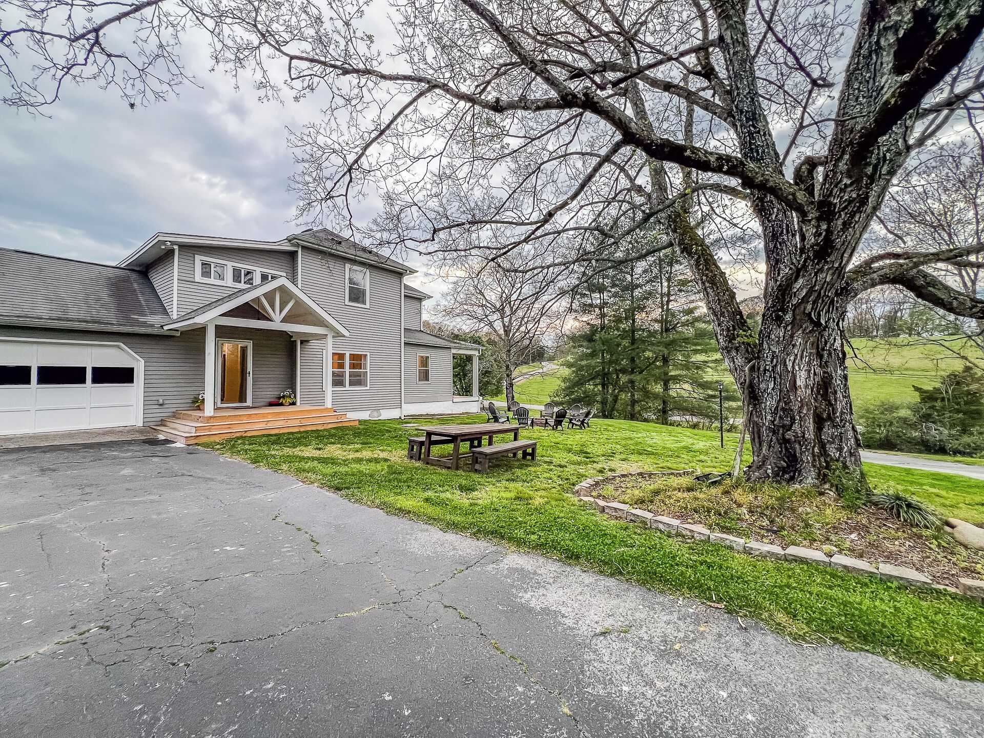 A residential house with a garage, a front porch, and a large tree in the yard.