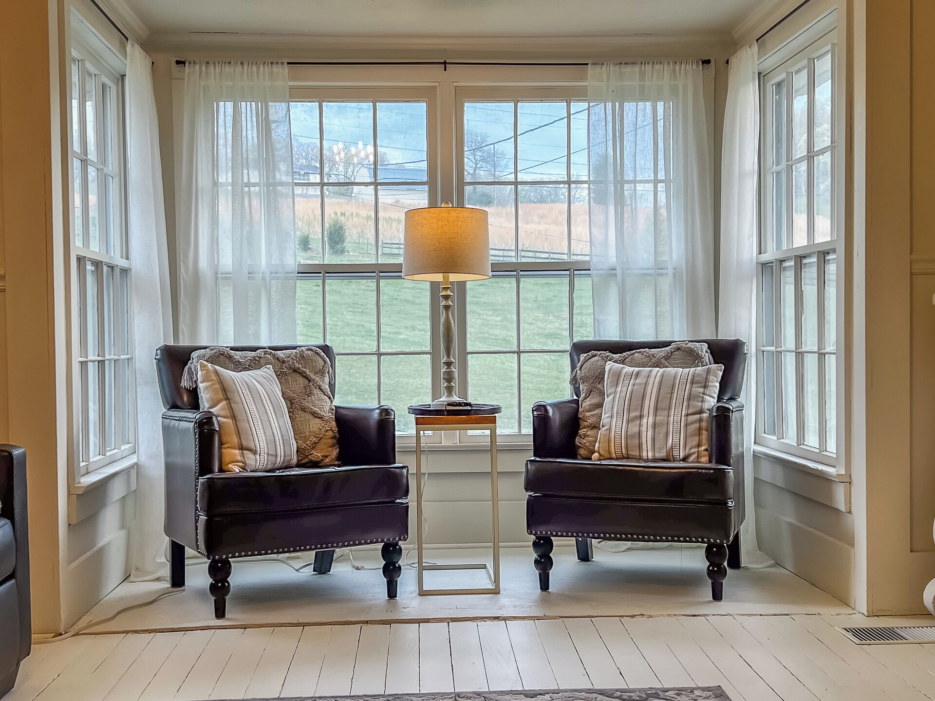 A room with two leather armchairs, a small table, and a lamp. There are large windows with curtains.