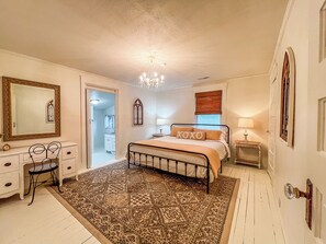 A bedroom with a bed, a desk, a chair, a chandelier, and a patterned rug.