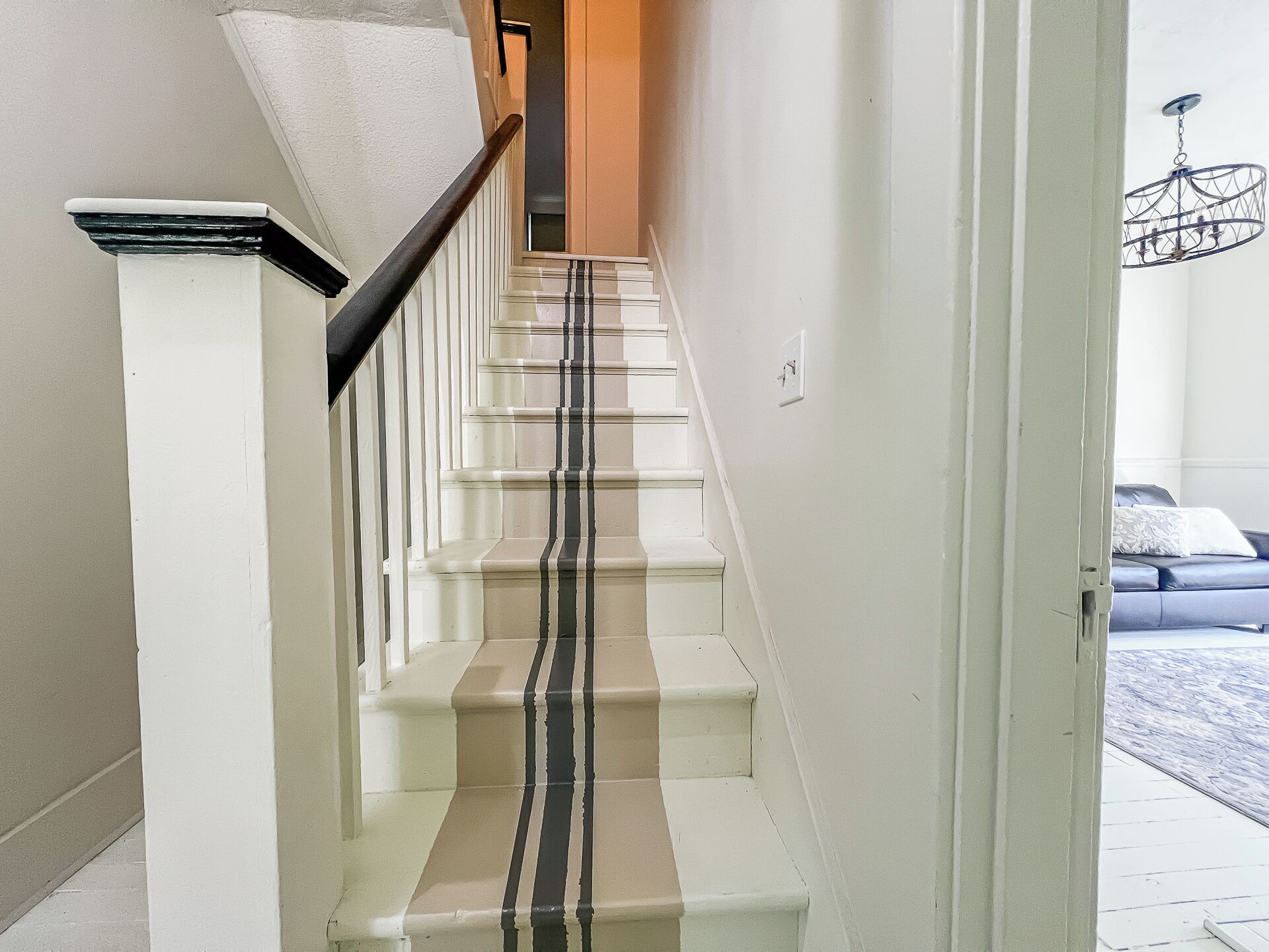 Un escalier dont les marches alternent entre le blanc et le beige, une main courante noire et un interrupteur sur le mur.