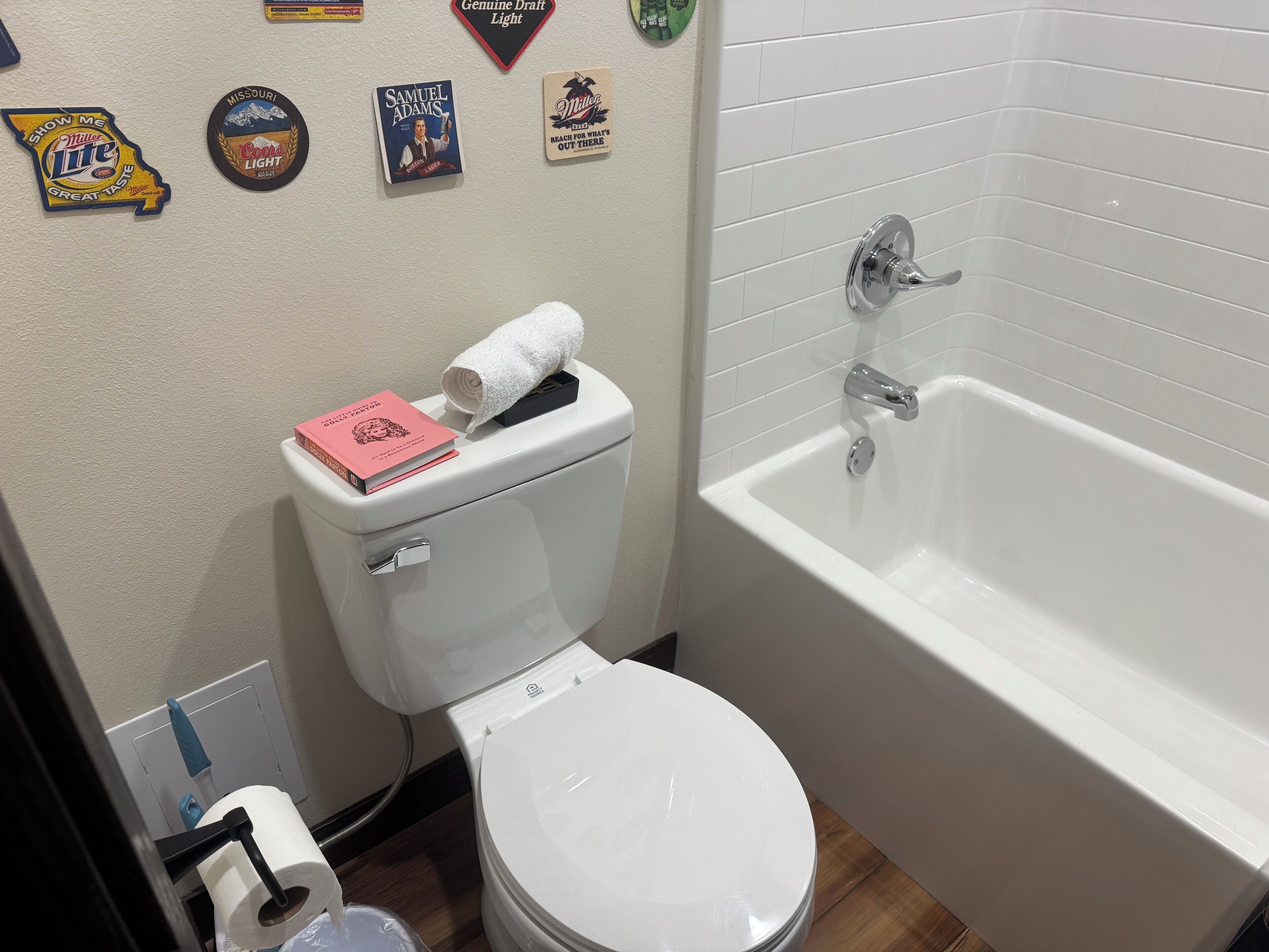 A bathroom with a toilet, a bathtub, and various wall decorations including beer bottle labels and a book.