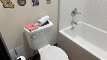 A bathroom with a toilet, a bathtub, and various wall decorations including beer bottle labels and a book.