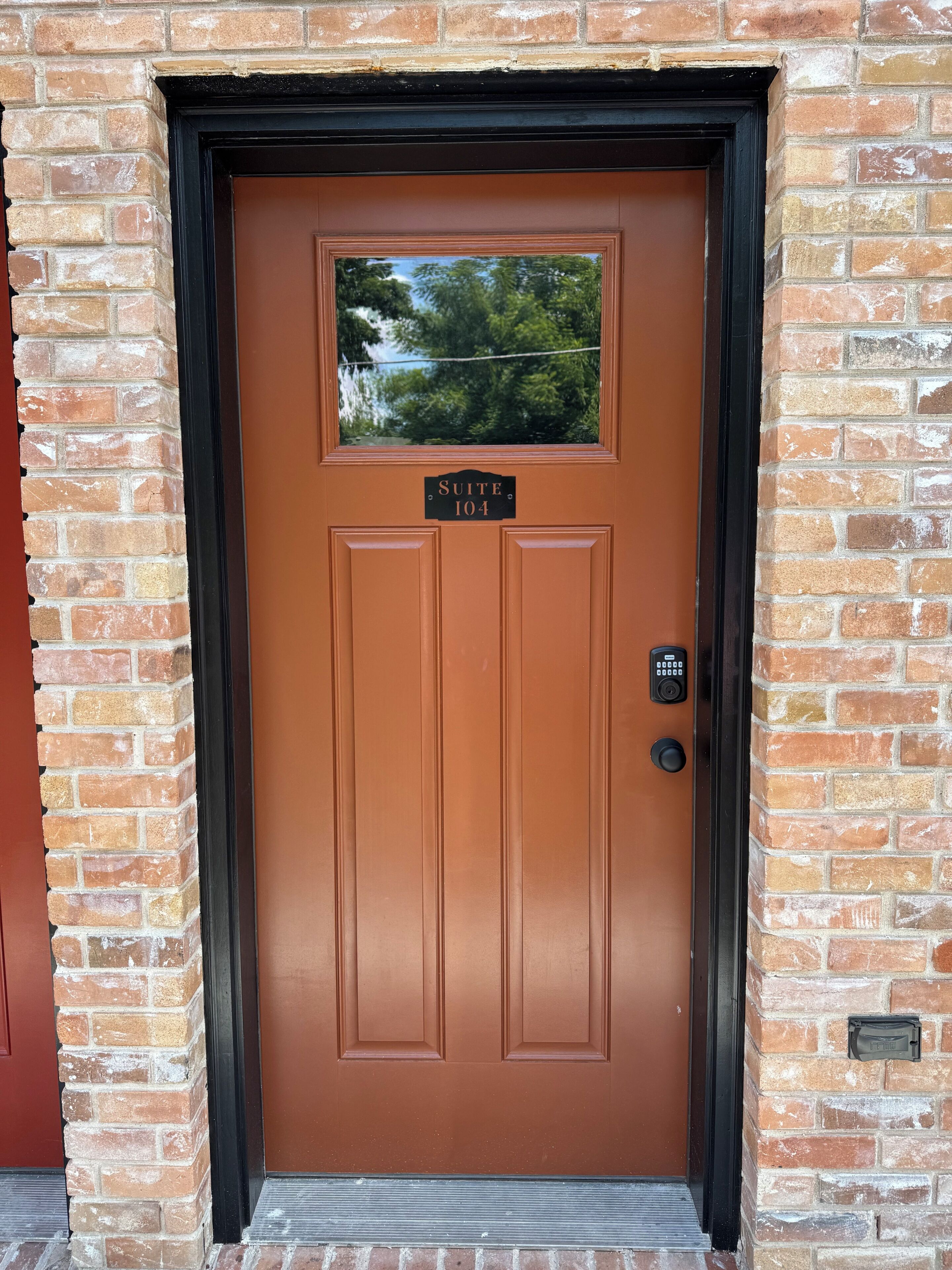 A brown door with a window above it, a keypad lock, and a sign that reads 'SUITE 104'.
