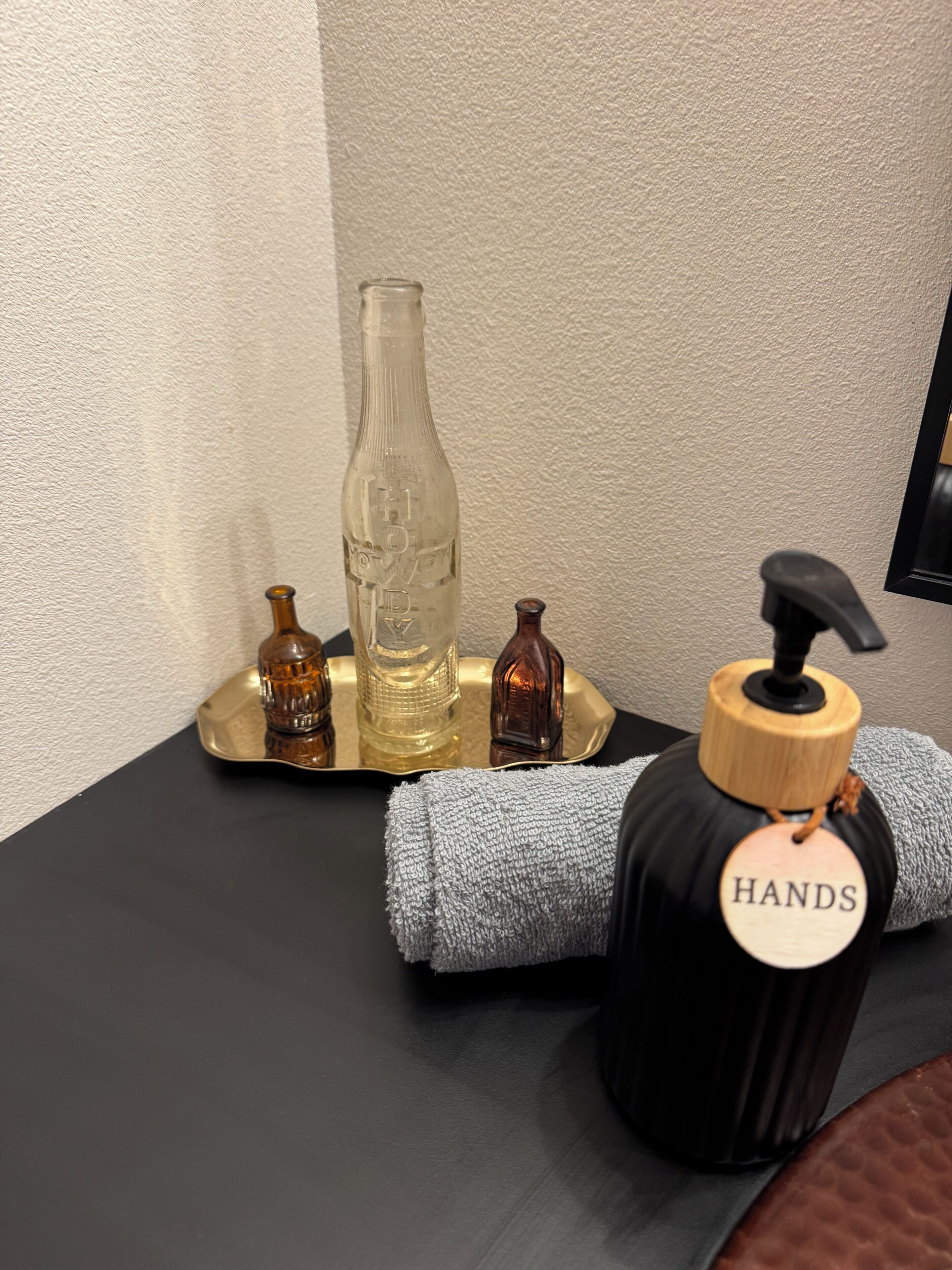 Ein Badezimmer-Waschtisch mit einer Seifenspenderflasche, einem Handtuch und zwei kleinen Flaschen.