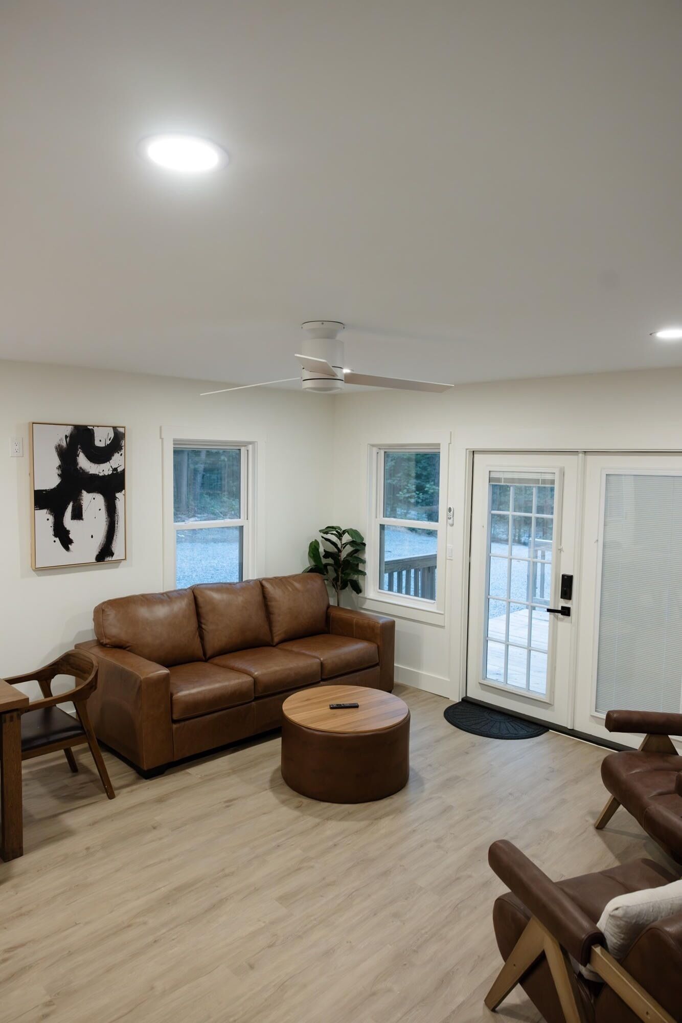 A living room with a brown leather sofa, a round ottoman, a wooden coffee table, and a ceiling fan.