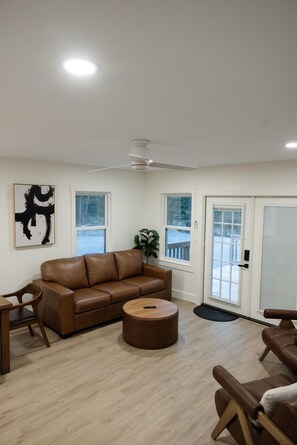 A living room with a brown leather sofa, a round ottoman, a wooden coffee table, and a ceiling fan.