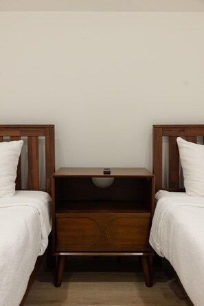 A room with two single beds, a nightstand with a lamp, and a plain wall.