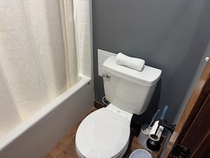 A small bathroom with a white toilet, a shower curtain, and a toilet brush.