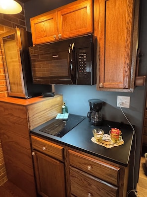 A compact kitchen with wooden cabinets, a black microwave, a coffee maker, and a small countertop.