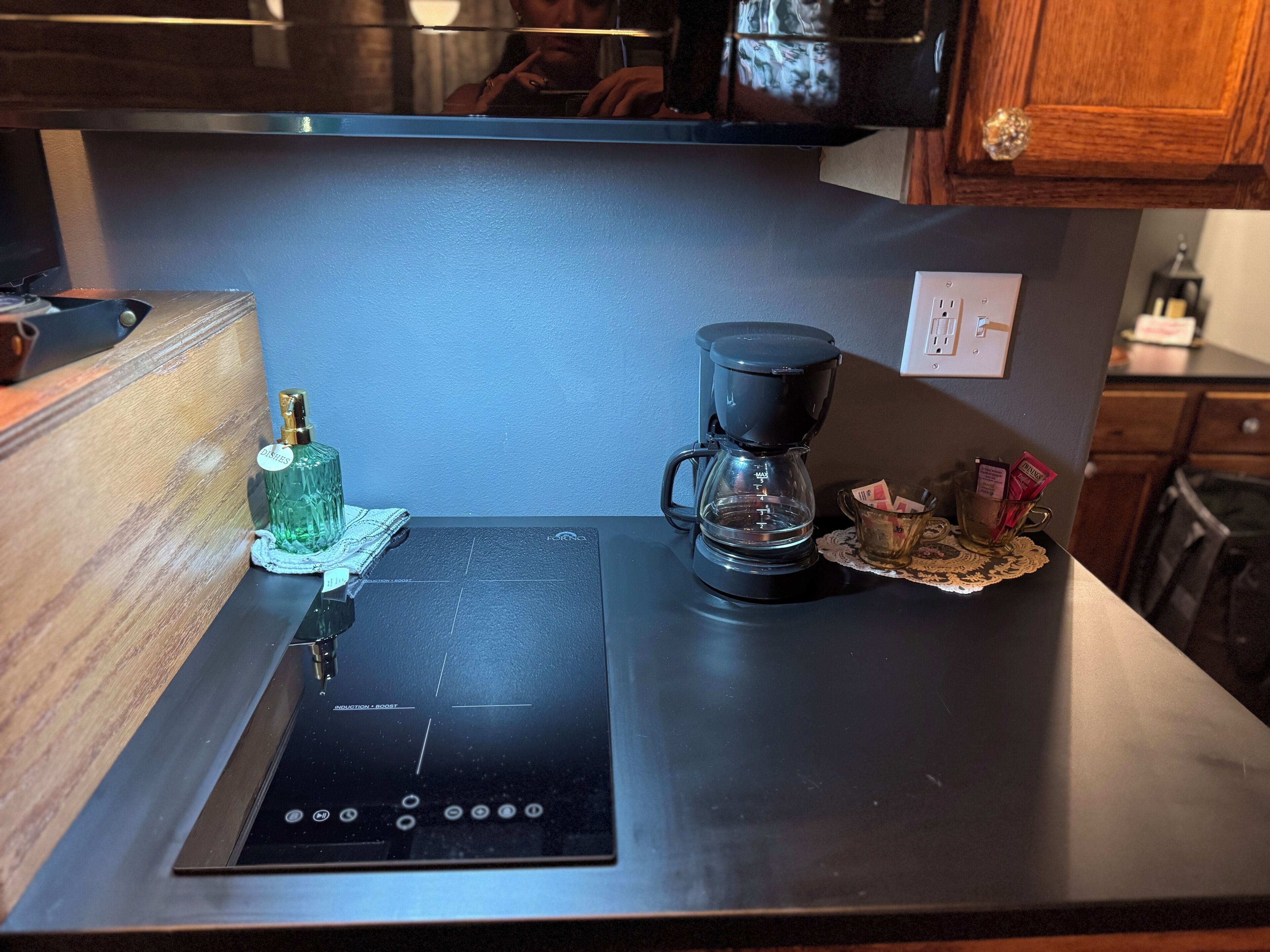 A kitchen counter with a black induction cooktop, a coffee maker, and a bottle of dish soap.