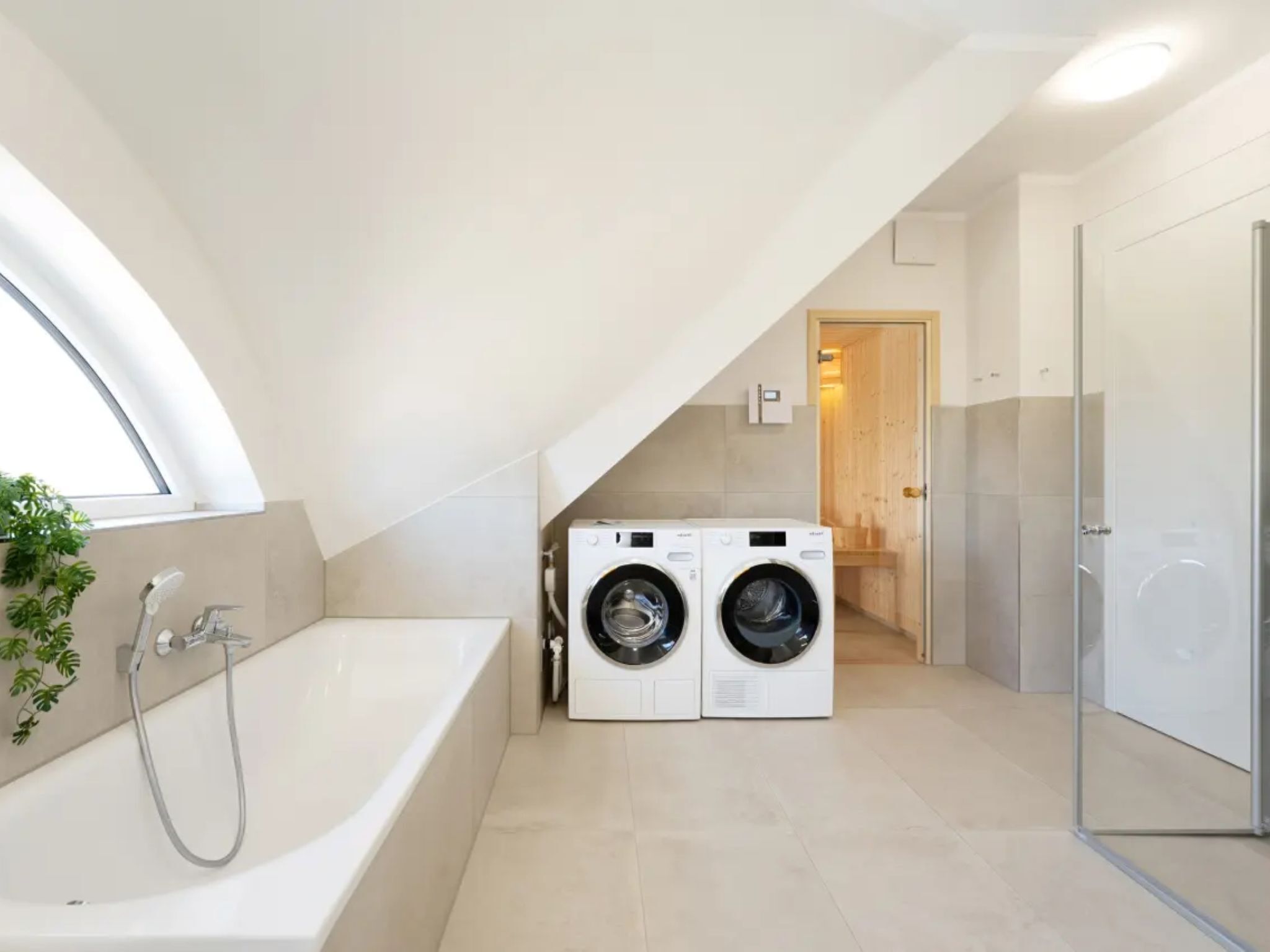 A modern bathroom with a bathtub, two wall-mounted washing machines, and a glass shower enclosure.