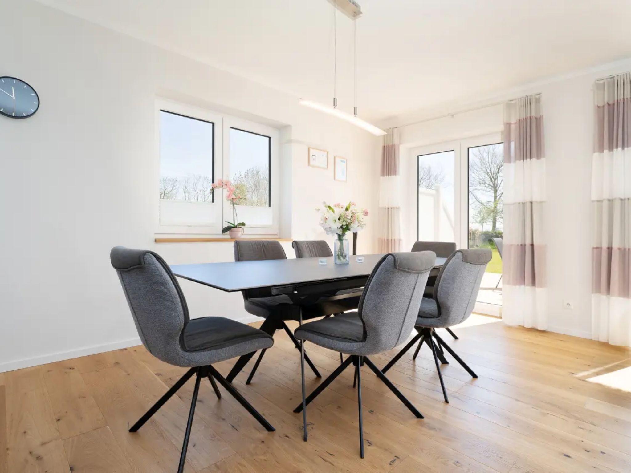 A modern dining area with a rectangular table, six grey chairs, and a vase of flowers.