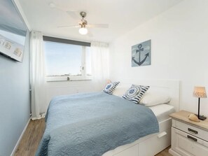 Un dormitori amb un llit, una nitòria, una làmpada, una finestra amb cortines i un ventilador de sostre.