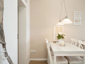 A dining area with a white table, chairs, a hanging light fixture, a wall-mounted mirror, and a decorative sign. - Meeresblick Ankerplatz 84 by Interhome (Kellenhusen)
