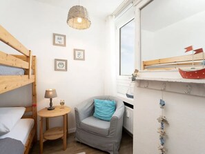 Una habitació petita i acollidora amb un llit superposat, un escriptori amb una làmpada, una cadira amb coixí i una finestra que dona a un vaixell.