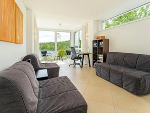 A modern living room with a sofa, a desk, and a chair. There is a large window with a view of greenery. - am Seeufer by Interhome (Malente-Gremsmühlen)