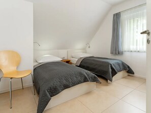 A bedroom with two beds, a chair, and a window with curtains. - am Seeufer by Interhome (Malente-Gremsmühlen)