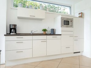 A modern kitchen with white cabinetry, a coffee maker, a microwave, and a window with a view of greenery. - am Seeufer by Interhome (Malente-Gremsmühlen)