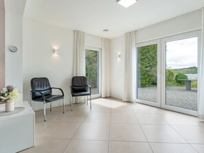 A spacious room with two black chairs, a white side table with a vase, and a large window offering a view of greenery. - am Seeufer by Interhome (Malente-Gremsmühlen)